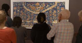 Visitors admire an 18th-century Buddhist priest's silk robe stitched with gold at "Intrinsic Beauty." (Lily Speredelozzi/GW Today)
